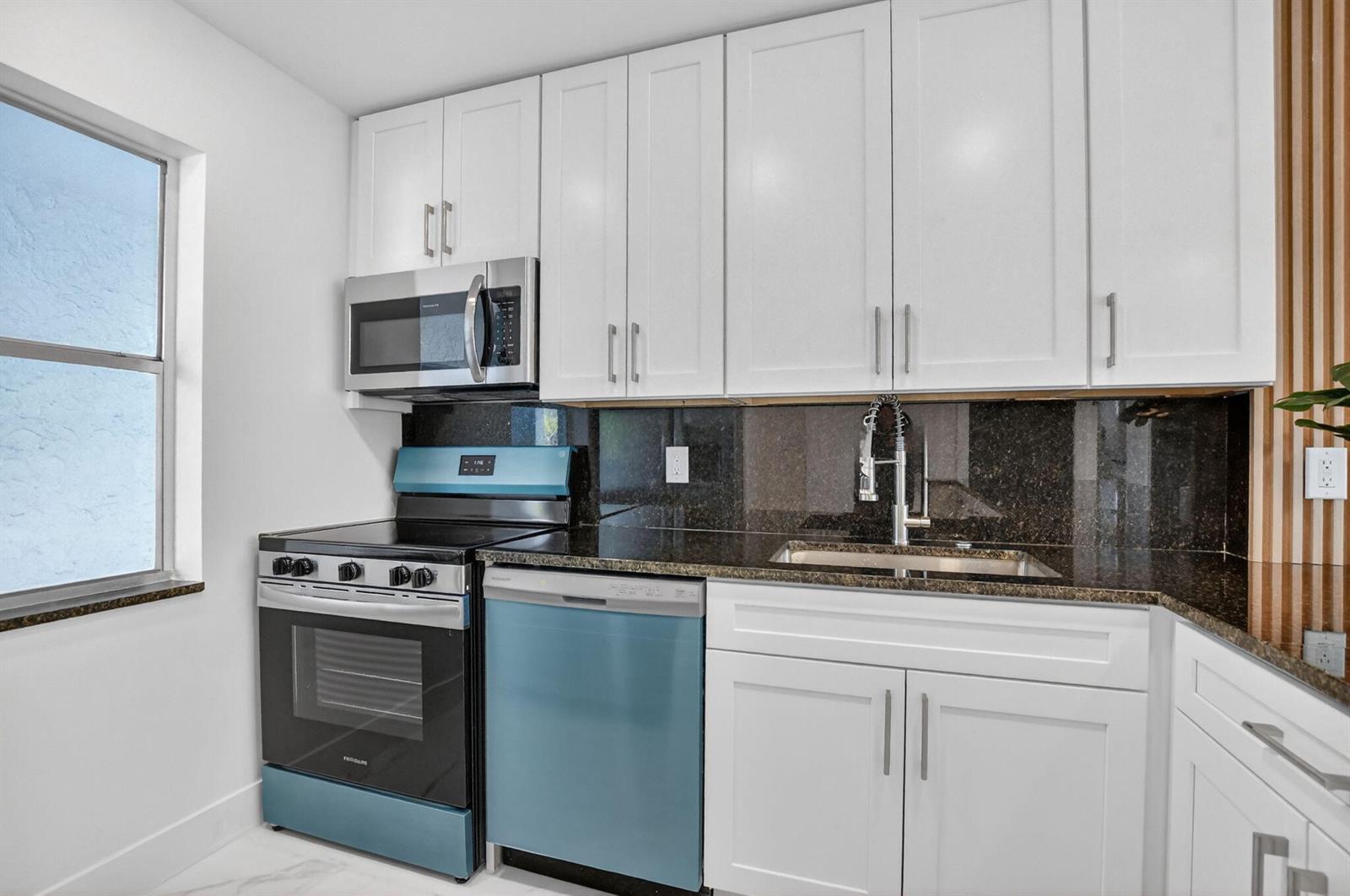 A kitchen features white cabinets, dark granite countertops, and blue-accented appliances — 9780 Marina Boulevard # 425, Boca Raton FL 33428, BOCA RATON, FL