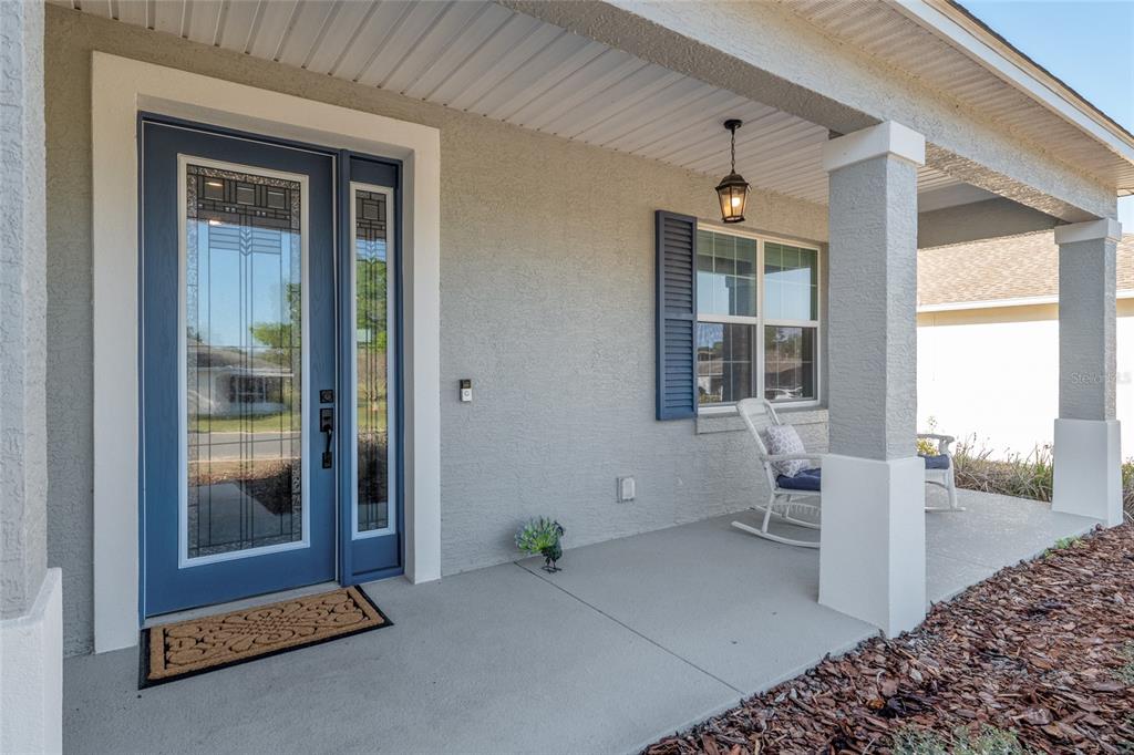 A covered front porch features a blue door with glass panels and two rocking chairs — 9922 SW 97TH LANE, OCALA, FL