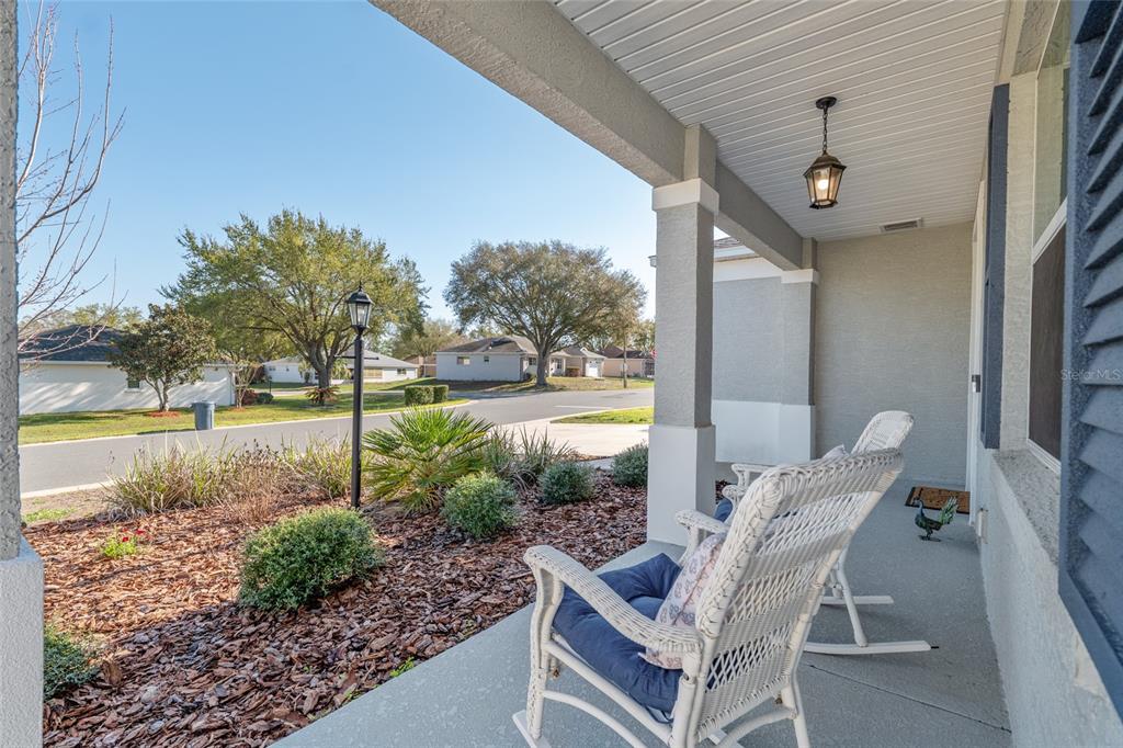 A covered front porch features two white wicker rocking chairs and a landscaped front yard — 9922 SW 97TH LANE, OCALA, FL