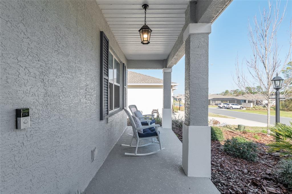 A covered front porch features gray stucco walls, two white rocking chairs, and a hanging lantern — 9922 SW 97TH LANE, OCALA, FL