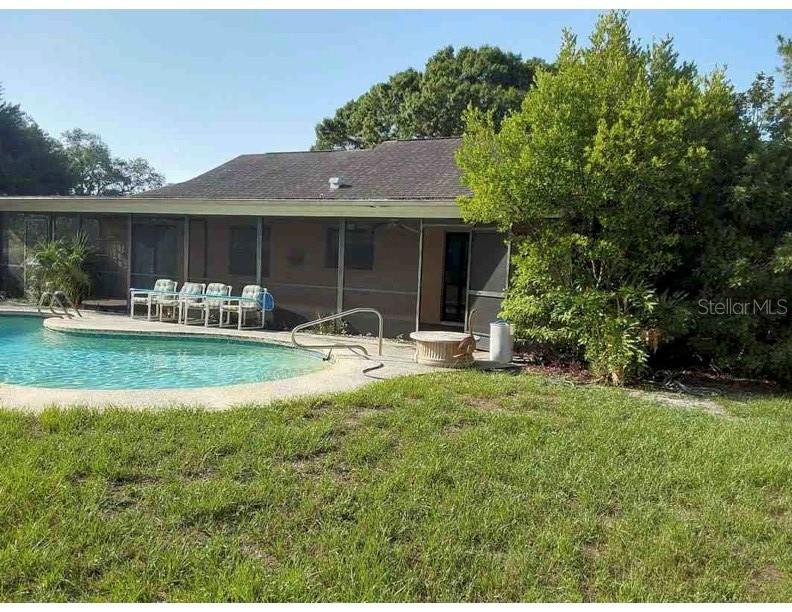 A backyard view of a house with a swimming pool and a screened-in patio — 7250 WOODBROOK DR, TAMPA, FL