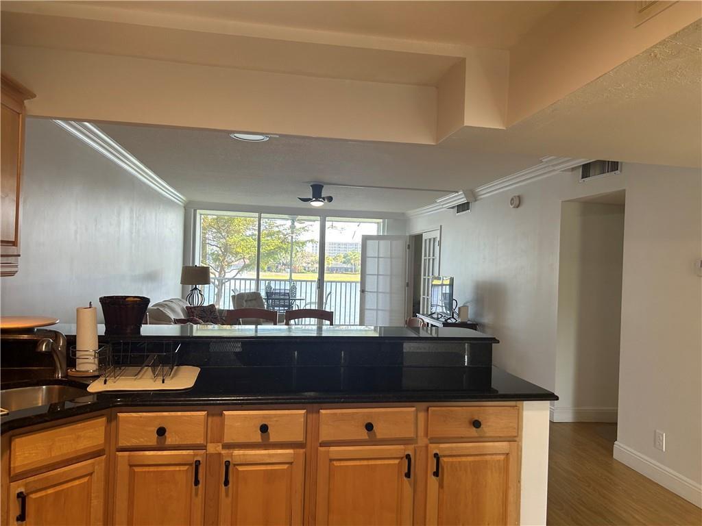 A kitchen with wood cabinets and black countertops overlooks a living area with water views — 3150 N Course Lane # 207, Pompano Beach FL 33069, POMPANO BEACH, FL