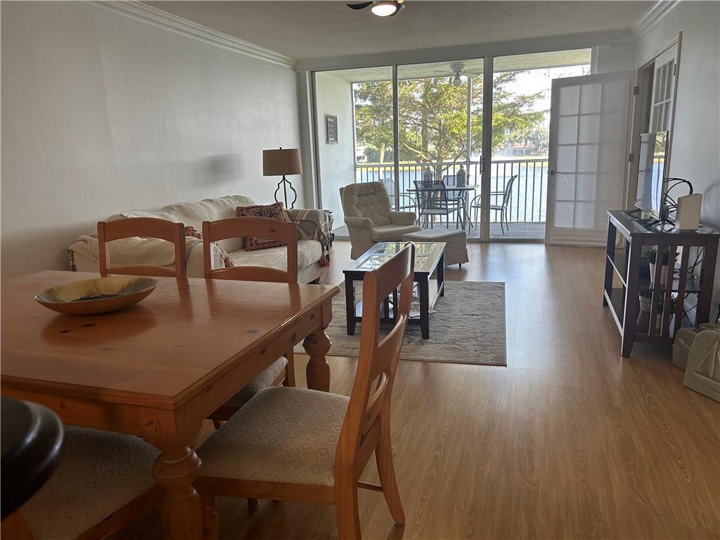 A dining area and living room with wood-look flooring lead to a screened balcony — 3150 N Course Lane # 207, Pompano Beach FL 33069, POMPANO BEACH, FL