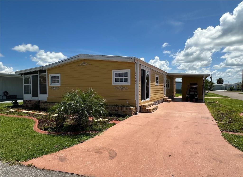 A yellow mobile home with a screened porch and a concrete driveway under a blue sky — 14700 Patrick Henry Road # 1, FL 33917, FL