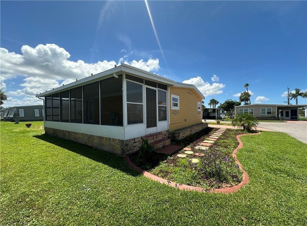 A yellow mobile home features a screened-in porch and a landscaped garden with stone pavers — 14700 Patrick Henry Road # 1, FL 33917, FL