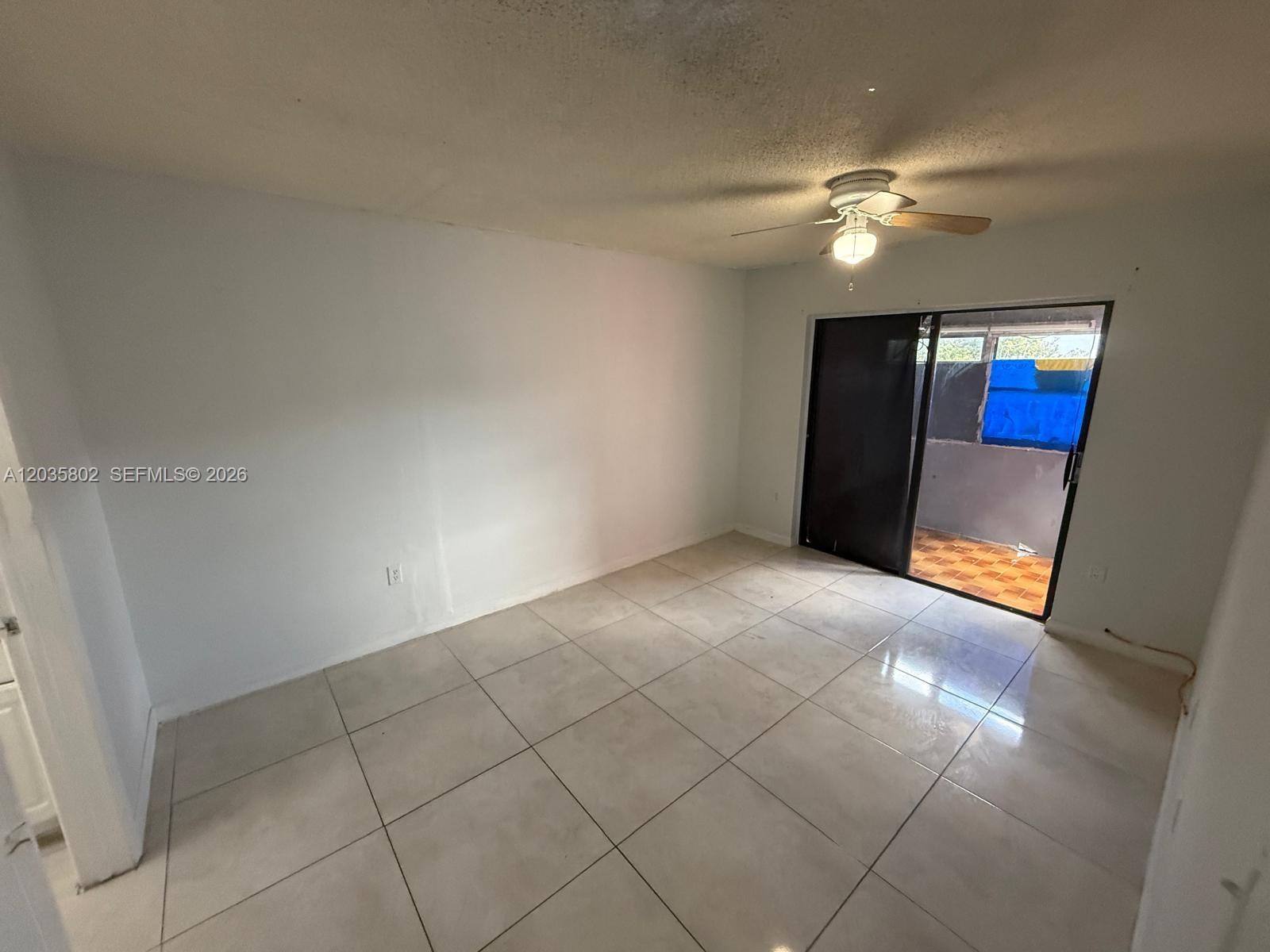 An empty room features white walls, large light-colored floor tiles, and a sliding glass door — 6675 W 4th Ave # 402, Hialeah FL 33012, HIALEAH, FL