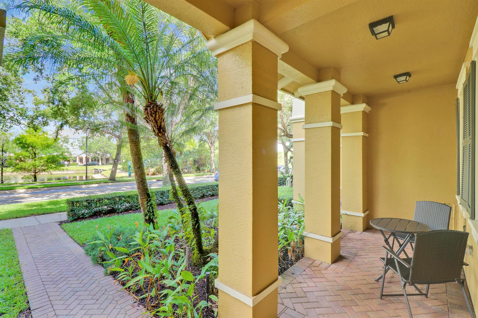 A covered brick patio features two chairs and a small table beside yellow support columns — 123 E Thatch Palm Circle, Jupiter FL 33458, JUPITER, FL