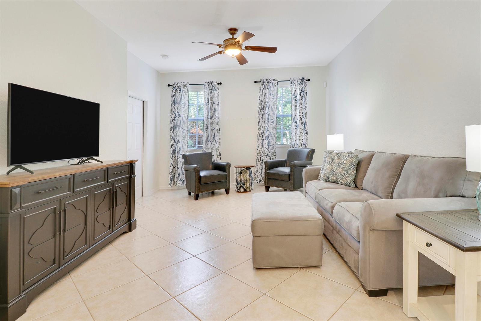 A living room features a grey sofa, two armchairs, a television console, and tile flooring — 123 E Thatch Palm Circle, Jupiter FL 33458, JUPITER, FL