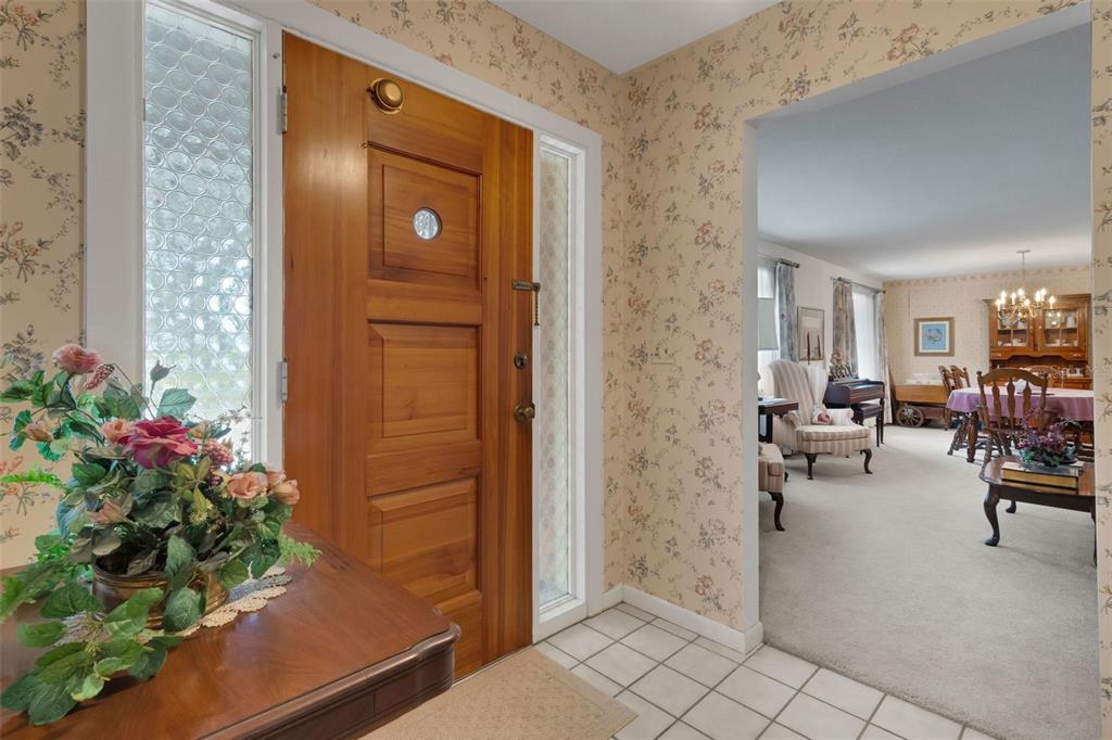 An entryway with floral wallpaper, a wooden front door, and a view into a dining room — 402 ABERDEEN COURT N, LAKELAND, FL
