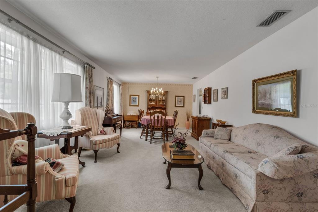 A living and dining room area features carpeted floors, traditional furniture, and a large window — 402 ABERDEEN COURT N, LAKELAND, FL