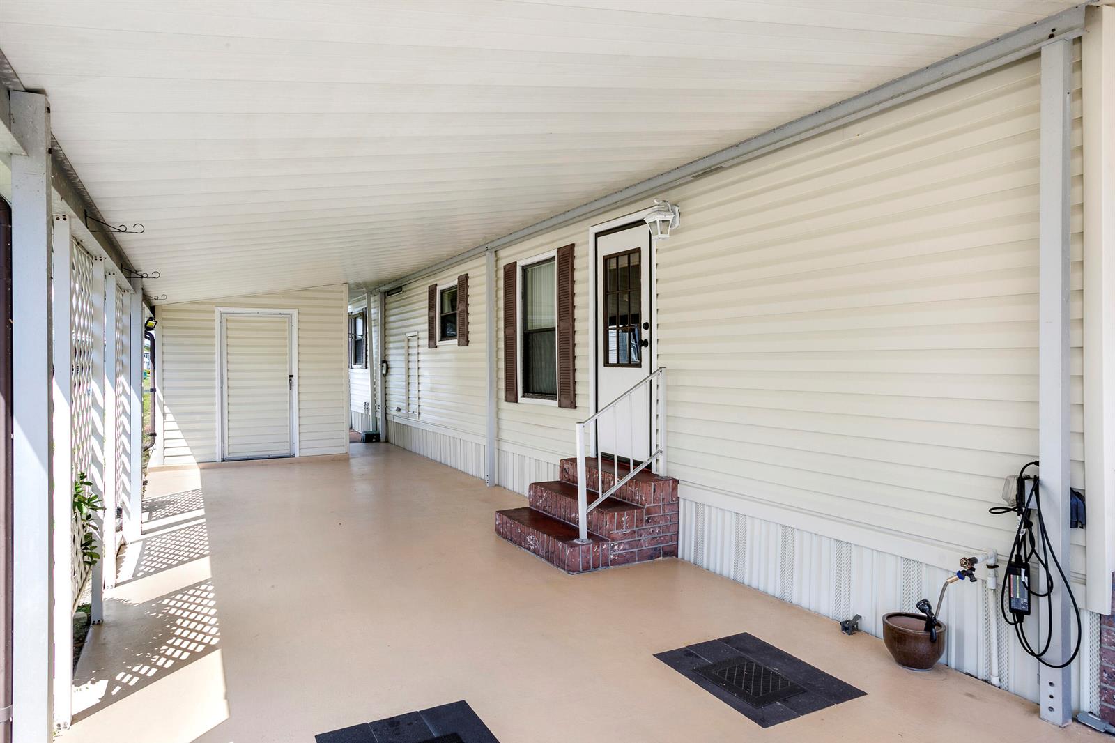A covered carport with beige siding, brick steps, and a white door leads to a home — 48014 Jaruco Bay, Boynton Beach FL 33436, BOYNTON BEACH, FL