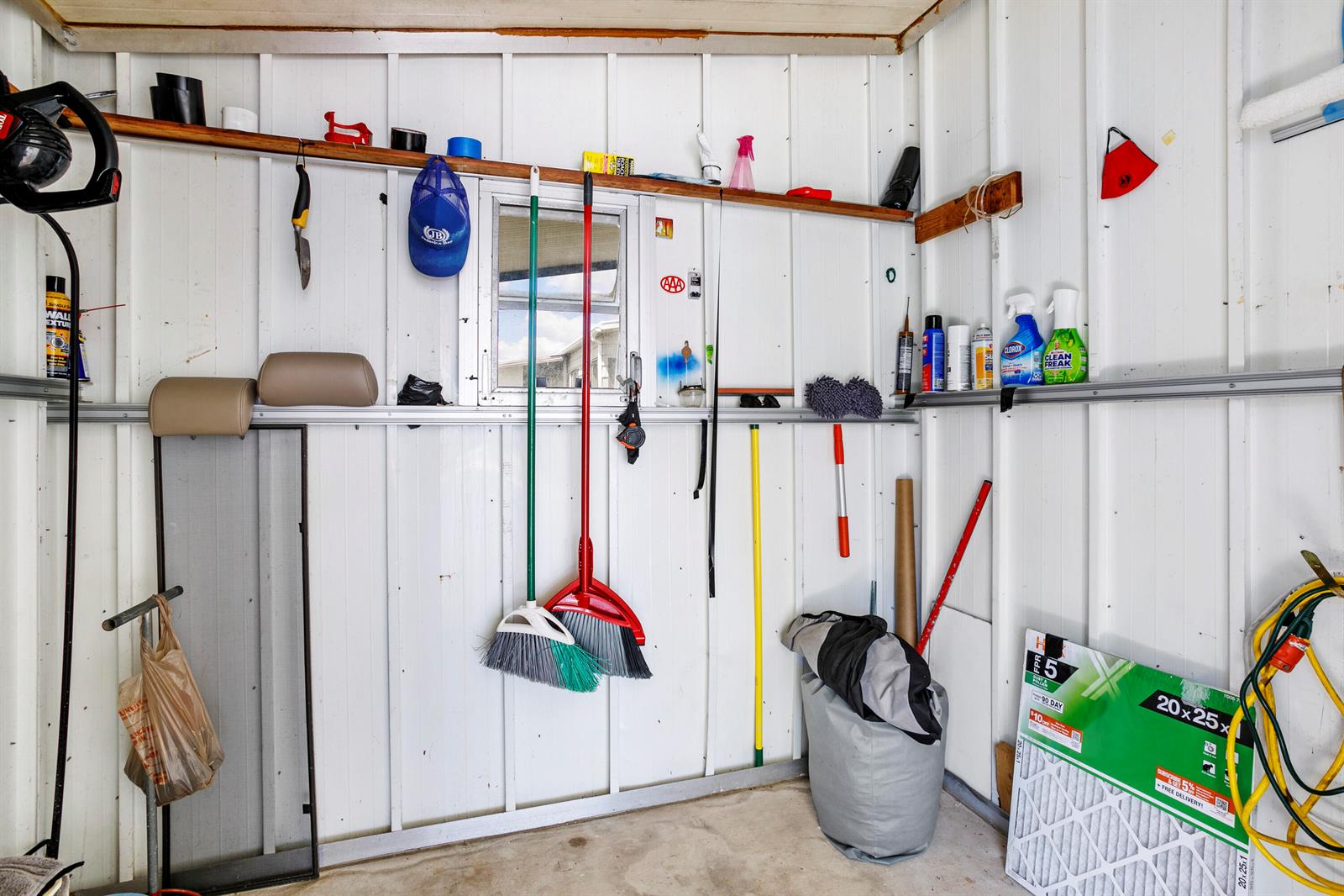 A storage shed interior features white vertical wall panels, a wooden shelf, and various tools — 48014 Jaruco Bay, Boynton Beach FL 33436, BOYNTON BEACH, FL