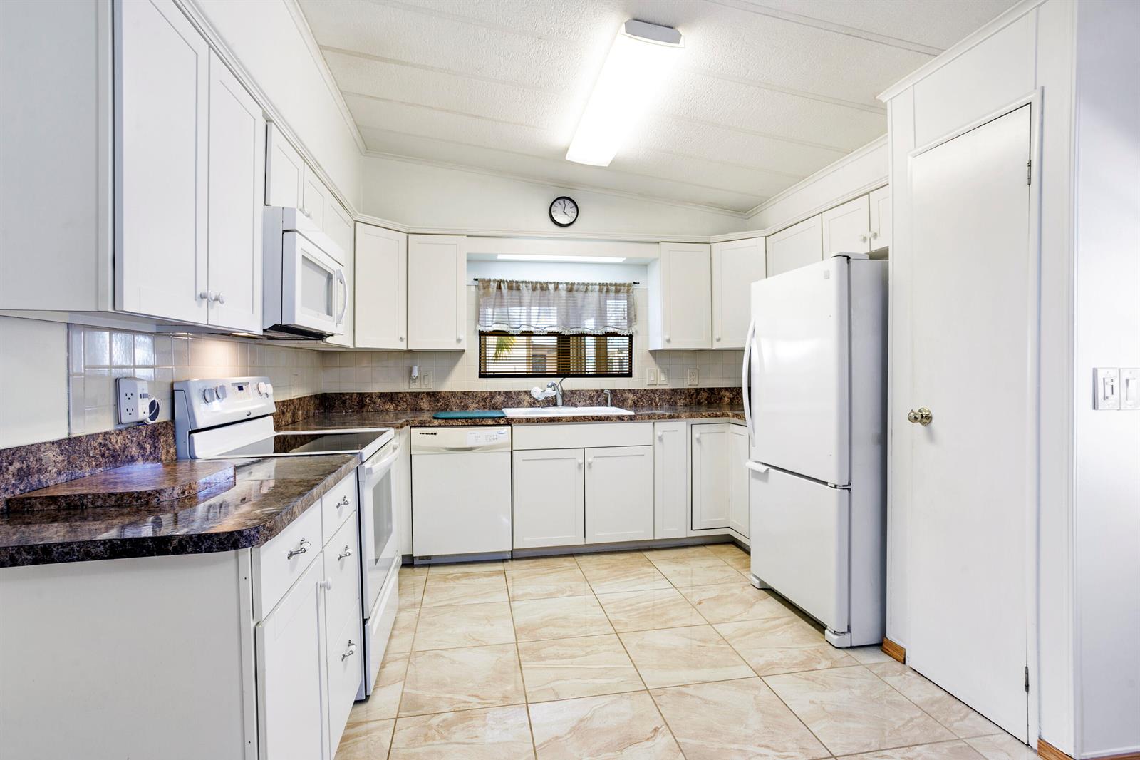 A kitchen with white cabinets, dark countertops, white appliances, and light-colored tile flooring — 48014 Jaruco Bay, Boynton Beach FL 33436, BOYNTON BEACH, FL