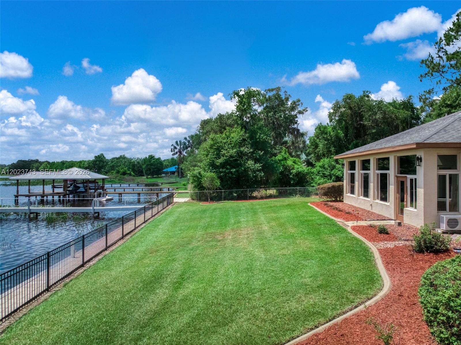 A grassy backyard overlooks a lake with a private dock and a house exterior — 9526 Kingfisher PL, Sebring FL 33875, SEBRING, FL
