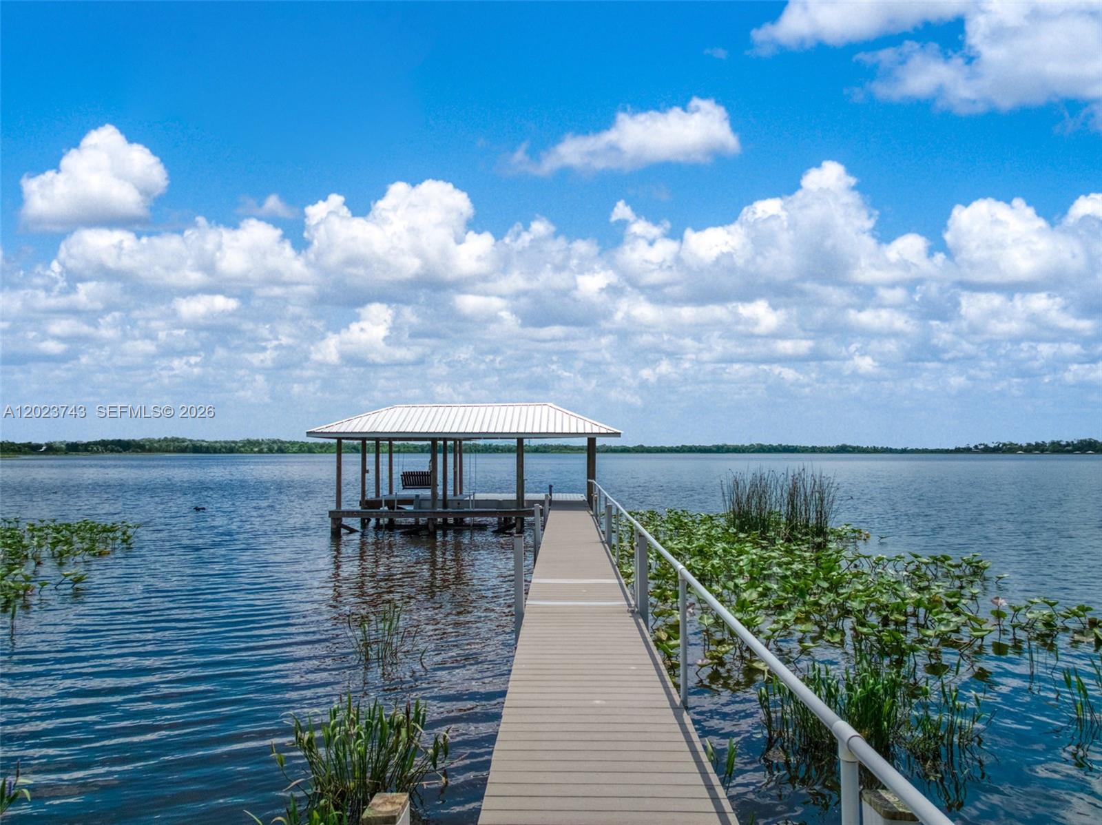 A wooden dock with a covered boat slip extends into a lake under a cloudy sky — 9526 Kingfisher PL, Sebring FL 33875, SEBRING, FL