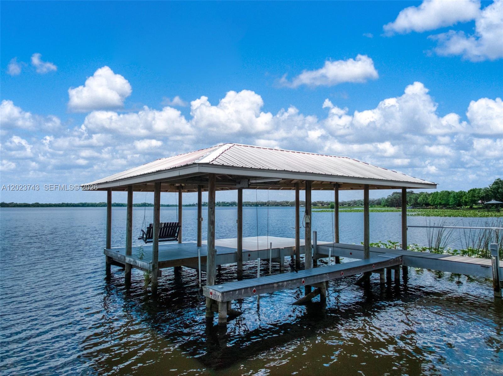 A wooden boat dock with a metal roof sits over a lake under a blue sky — 9526 Kingfisher PL, Sebring FL 33875, SEBRING, FL
