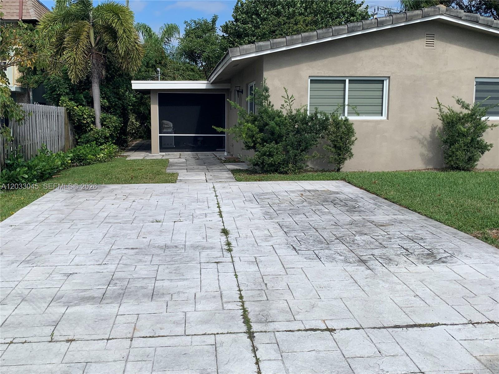 A concrete driveway leads to a house with a screened-in patio and landscaped yard — 491 SE 23rd Ave # 491, Pompano Beach FL 33062, POMPANO BEACH, FL