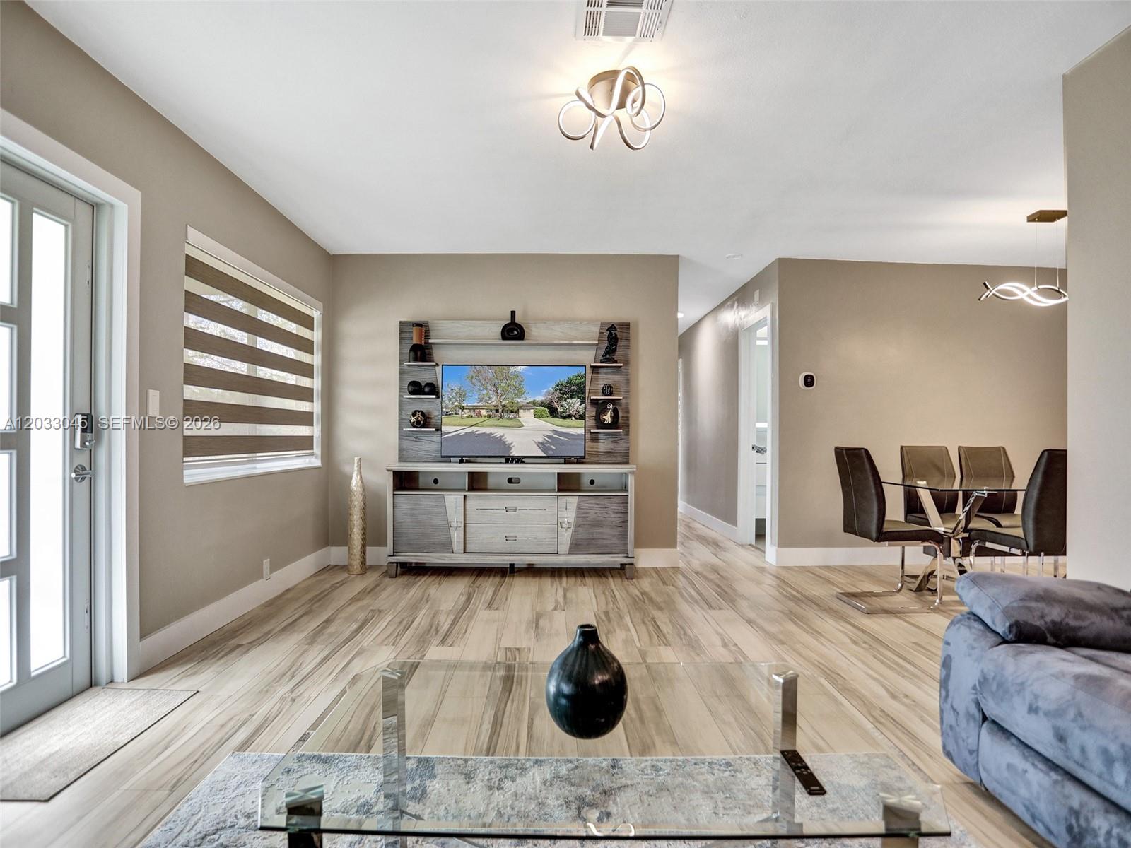 A living room features wood-look tile flooring, a media console, and an adjacent dining area — 491 SE 23rd Ave # 491, Pompano Beach FL 33062, POMPANO BEACH, FL