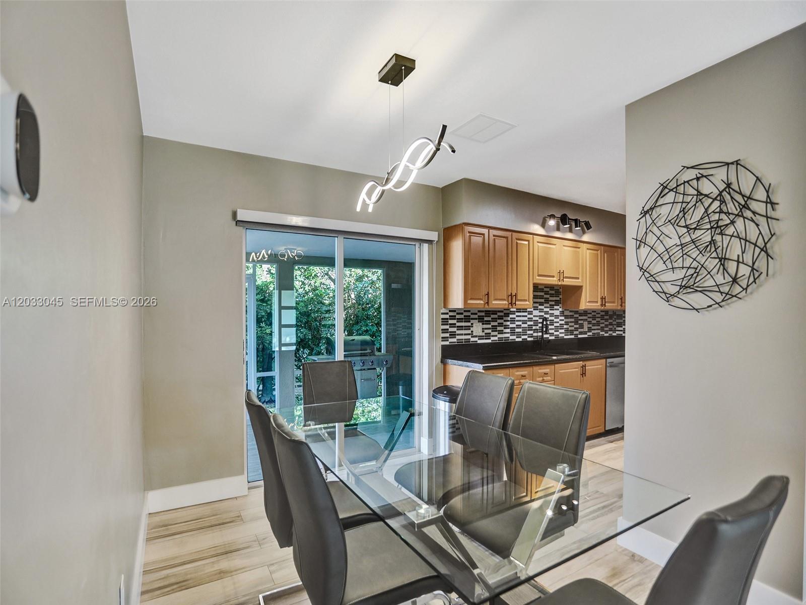 A dining area with a glass table and chairs sits adjacent to a kitchen with wood cabinets — 491 SE 23rd Ave # 491, Pompano Beach FL 33062, POMPANO BEACH, FL