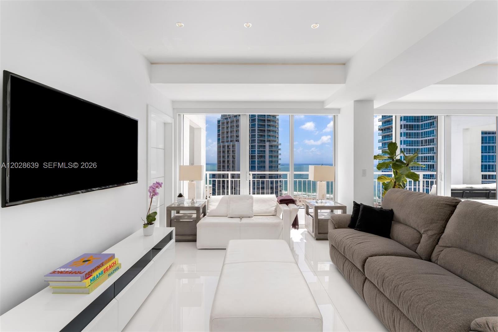 A bright living room features white tile floors, a large television, and floor-to-ceiling ocean views — 400 S Pointe Dr, Miami Beach FL 33139, MIAMI BEACH, FL