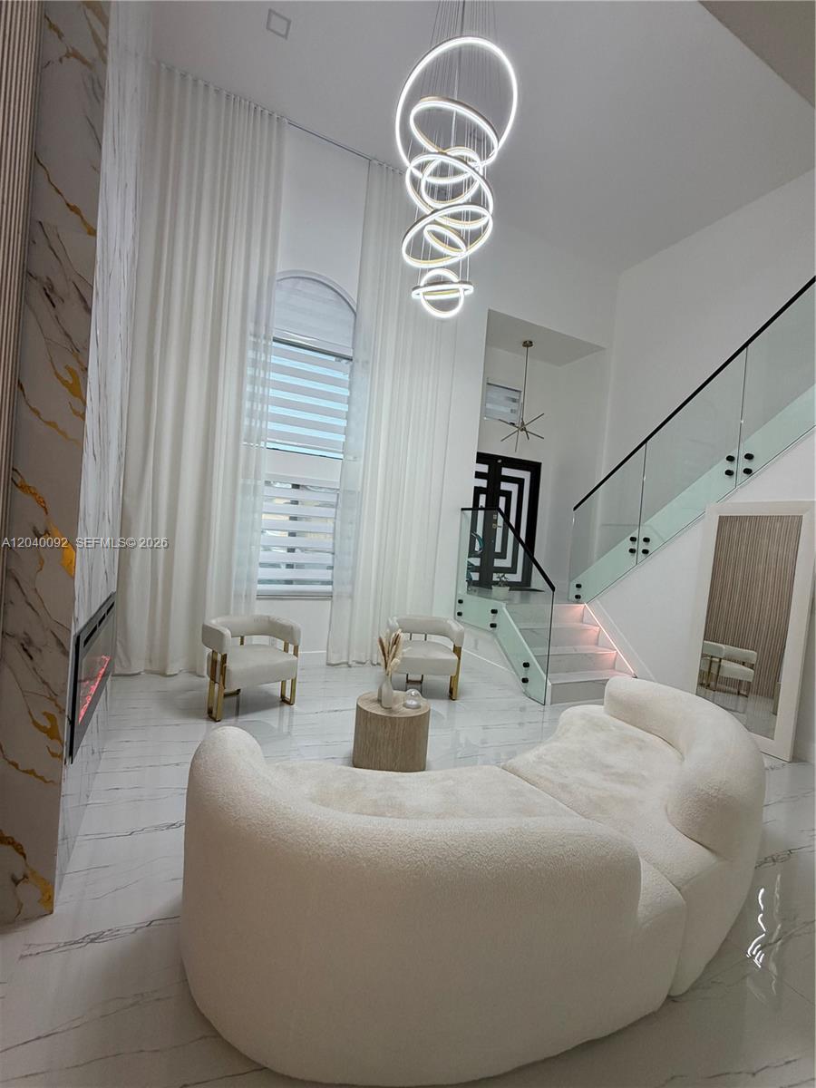 A modern living room features a curved sofa, two armchairs, a fireplace, and a chandelier — 854 NW 132nd Ct, Miami FL 33182, MIAMI, FL