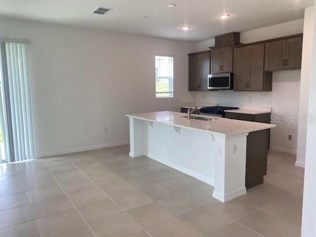 A kitchen features a white island, brown cabinets, and light-colored tile flooring — 27412 BLACK KITE AVENUE, HOWEY IN THE HILLS, FL