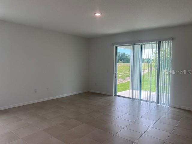 An empty room features light-colored tile flooring, white walls, and a sliding glass door — 27412 BLACK KITE AVENUE, HOWEY IN THE HILLS, FL