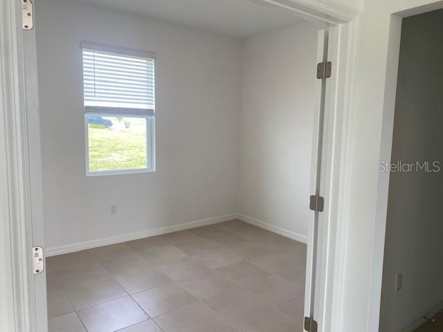 An empty room features light-colored tile flooring, white walls, and a window with blinds — 27412 BLACK KITE AVENUE, HOWEY IN THE HILLS, FL