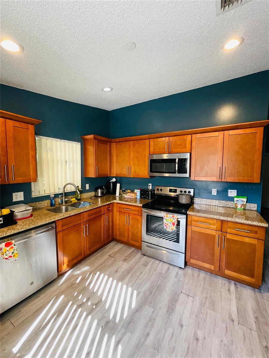 A kitchen features wood cabinets, granite countertops, stainless steel appliances, and dark blue walls — 244 Caribe Court, FL 33413, FL