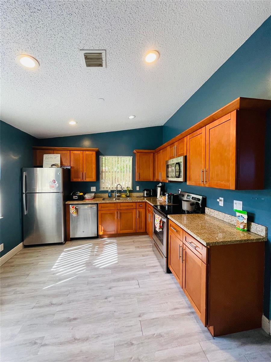 A kitchen features wood cabinets, granite countertops, stainless steel appliances, and dark blue walls — 244 Caribe Court, FL 33413, FL