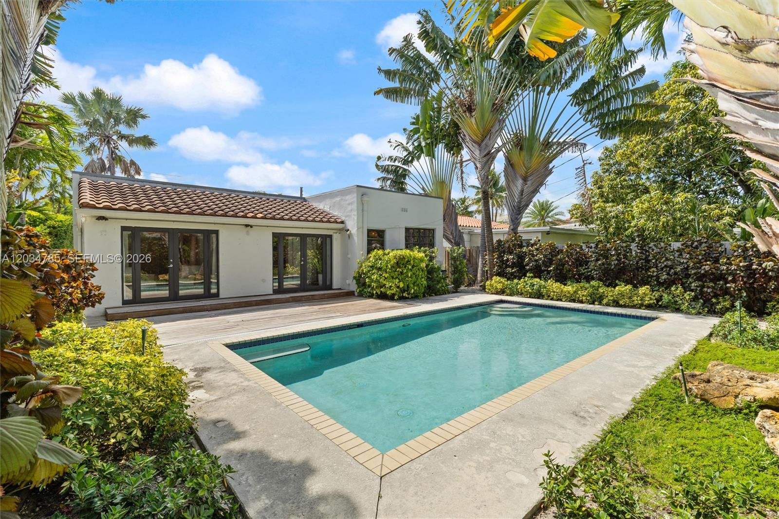 A backyard features a rectangular swimming pool, a wooden deck, and lush tropical landscaping — 4531 Sheridan Ave, Miami Beach FL 33140, MIAMI BEACH, FL