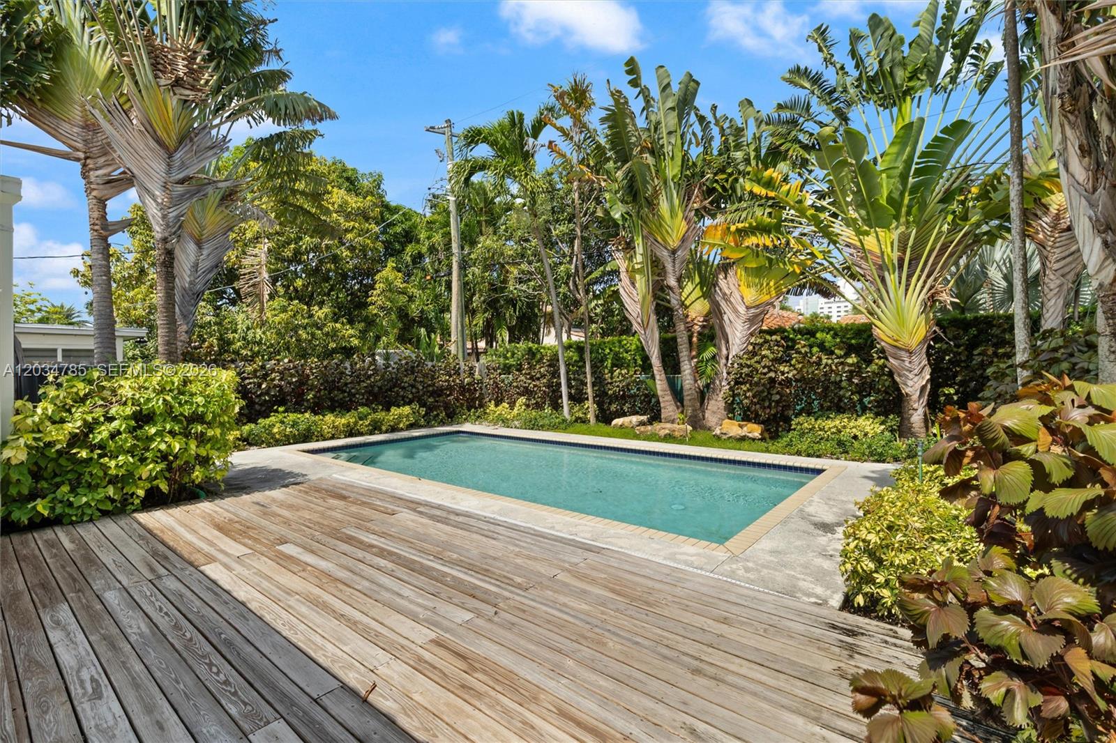 A rectangular swimming pool is surrounded by a wooden deck and lush tropical landscaping — 4531 Sheridan Ave, Miami Beach FL 33140, MIAMI BEACH, FL