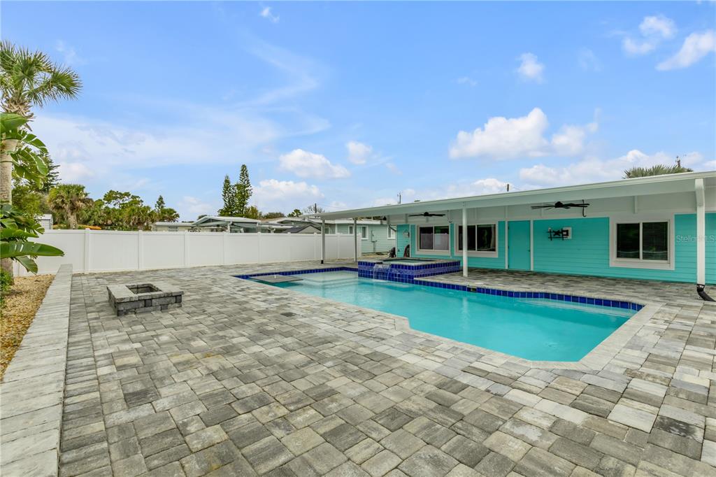 A backyard features a rectangular swimming pool with a spa, stone pavers, and a white fence — 921 E 2ND AVENUE, NEW SMYRNA BEACH, FL
