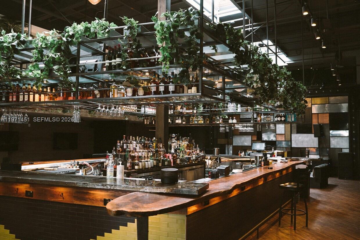 A bar area features a wooden counter, metal shelving with hanging plants, and bottle displays — 150 NW 24th St, Miami FL 33127, MIAMI, FL