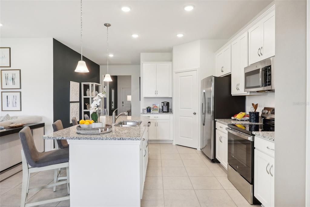 A modern kitchen features white cabinets, granite countertops, stainless steel appliances, and a central island — 9517 STARLING LOOP, LEESBURG, FL