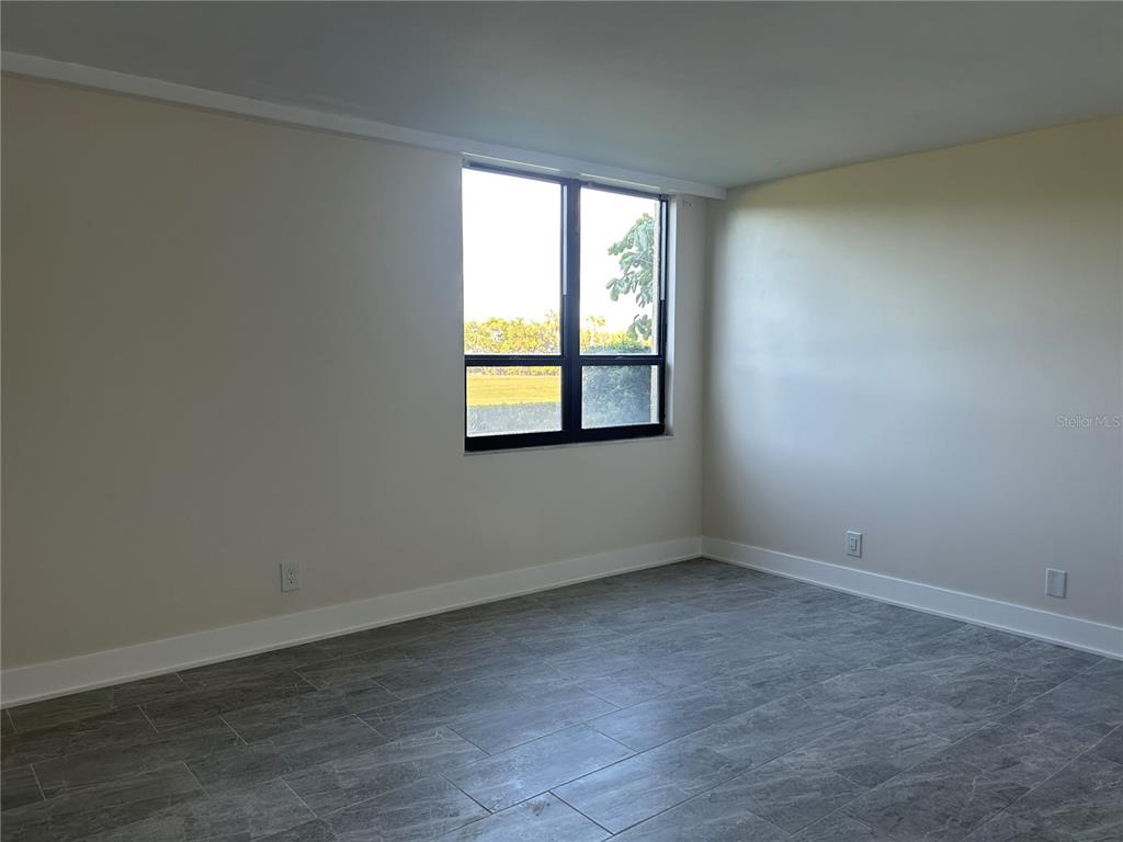 An empty room features light-colored walls, gray tile flooring, and a single window — 2618 COVE CAY DRIVE UNIT 103, CLEARWATER, FL