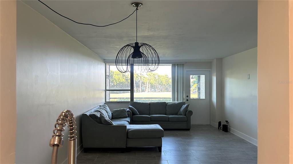 A living room features a gray sectional sofa, a modern wire pendant light, and tile flooring — 2618 COVE CAY DRIVE UNIT 103, CLEARWATER, FL