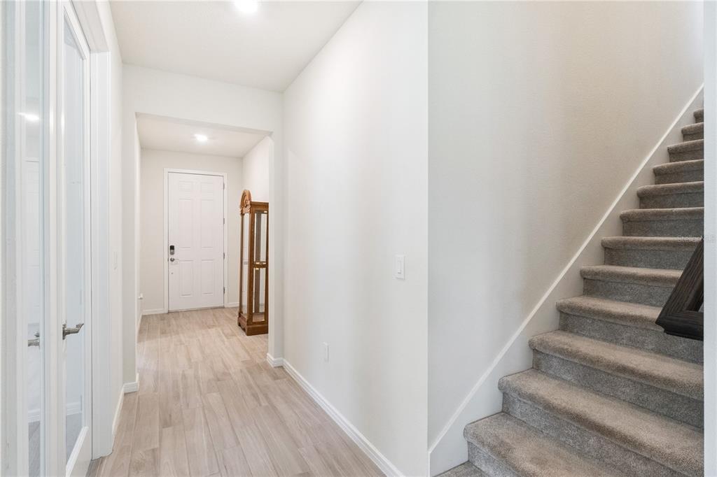 A bright entryway features light wood-look flooring, a white front door, and carpeted stairs — 2691 RIVER CREEK LANE, ST CLOUD, FL