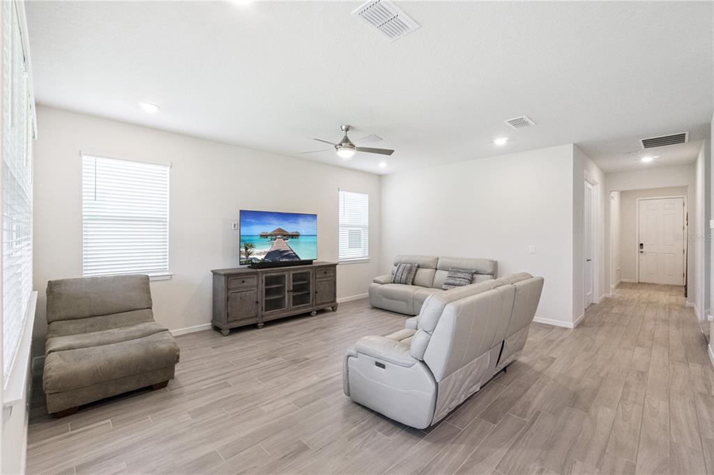 A living room with light wood-look tile flooring, gray furniture, and a wall-mounted television — 2691 RIVER CREEK LANE, ST CLOUD, FL