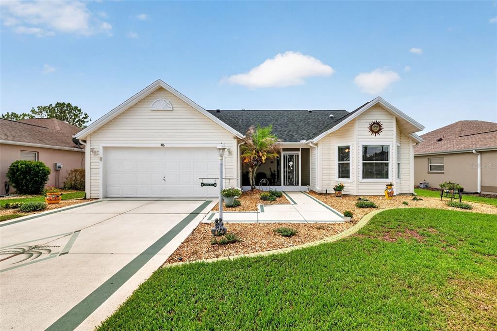 A single-story house with beige siding, a two-car garage, and a landscaped front yard — 416 CARRERA DRIVE, THE VILLAGES, FL
