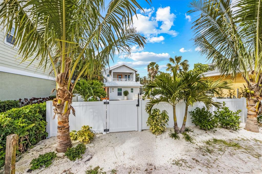 A white fence and palm trees frame a view of a two-story house — 112 CEDAR AVENUE, ANNA MARIA, FL