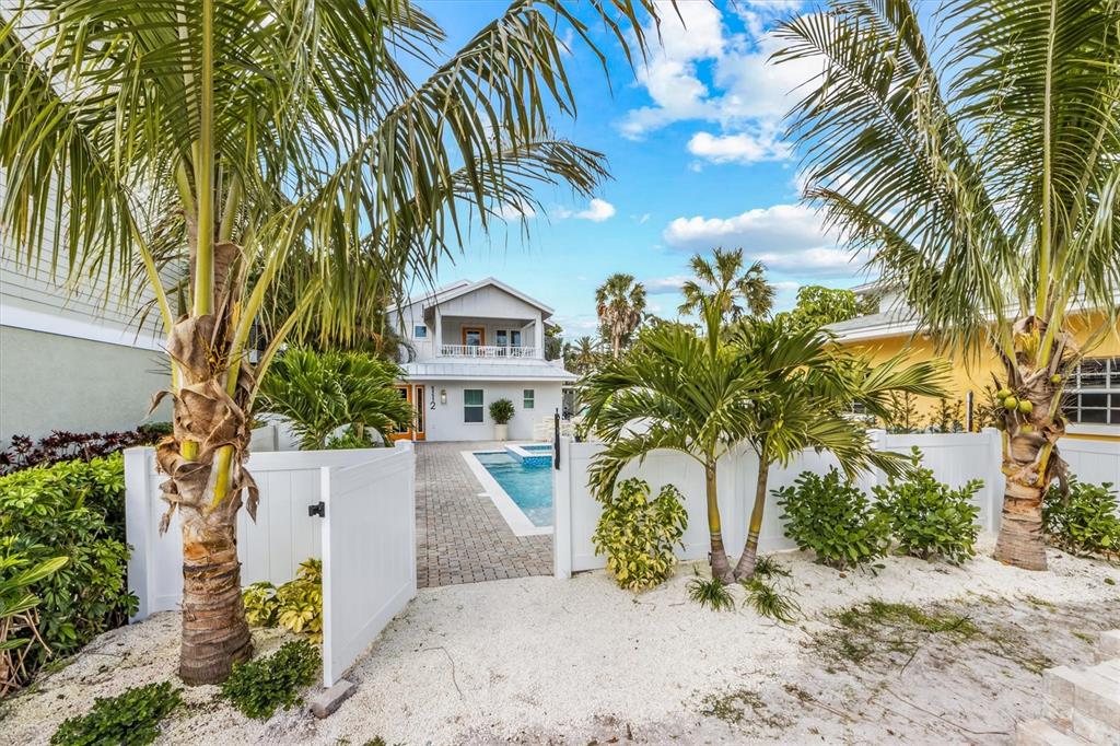 A white fence surrounds a backyard pool area with palm trees and a paved patio — 112 CEDAR AVENUE, ANNA MARIA, FL