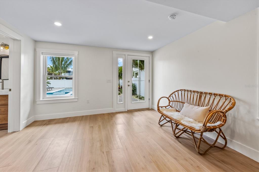 A bright room features light wood flooring, a rattan bench, and a door to a pool — 112 CEDAR AVENUE, ANNA MARIA, FL
