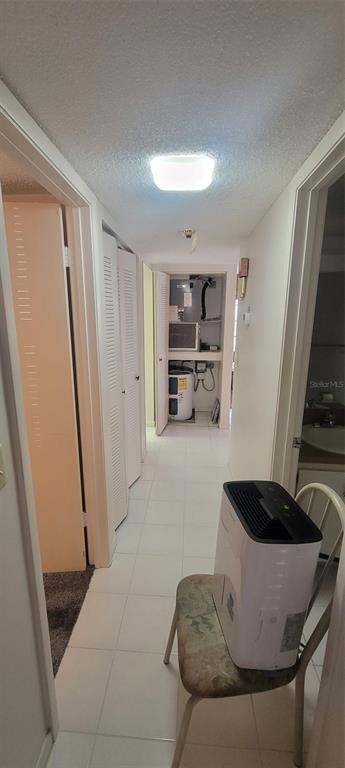 A hallway with white tile flooring leads to a utility closet containing a water heater — 180 MAGNOLIA WOODS COURT UNIT 19A, DELTONA, FL