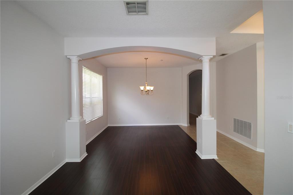 A dining room features dark wood flooring, an arched entryway with columns, and a chandelier — 9885 LELAND DRIVE, ORLANDO, FL