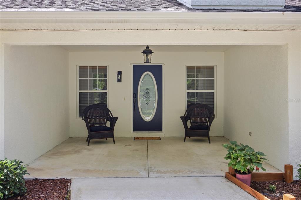 A covered front porch features a blue door, two wicker chairs, and two windows — 7050 NE STATE ROAD 121, WILLISTON, FL