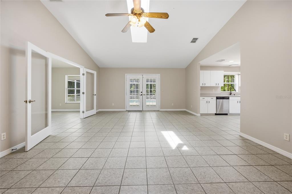 A spacious room with tiled floors, a ceiling fan, French doors, and an adjacent kitchen — 7050 NE STATE ROAD 121, WILLISTON, FL