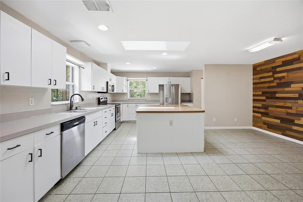A kitchen features white cabinetry, a central island with a wood top, and a wood-paneled wall — 7050 NE STATE ROAD 121, WILLISTON, FL