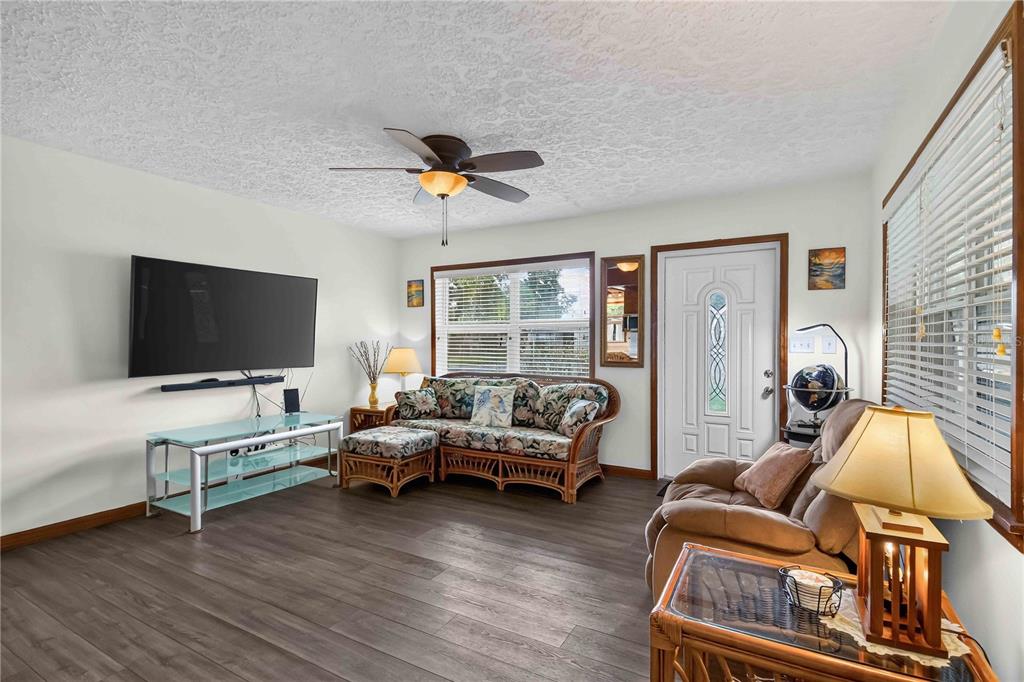 A living room featuring a television, wicker sofa, recliner, and wood-look flooring — 4704 PARK ACRES DRIVE, BRADENTON, FL
