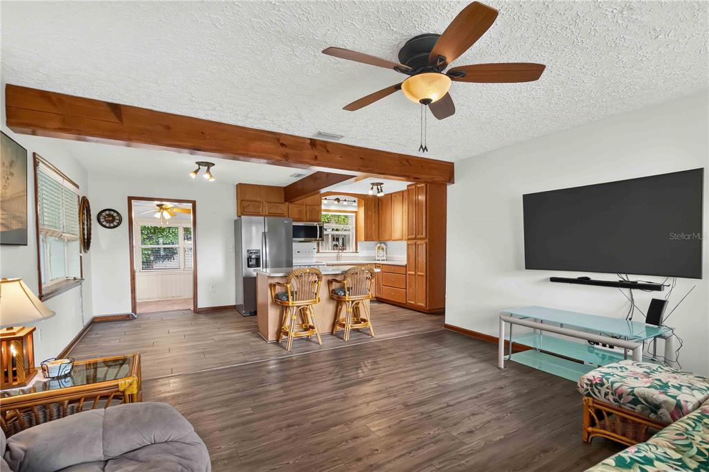 A living room and kitchen area with wood-look flooring, a ceiling fan, and wooden beams — 4704 PARK ACRES DRIVE, BRADENTON, FL